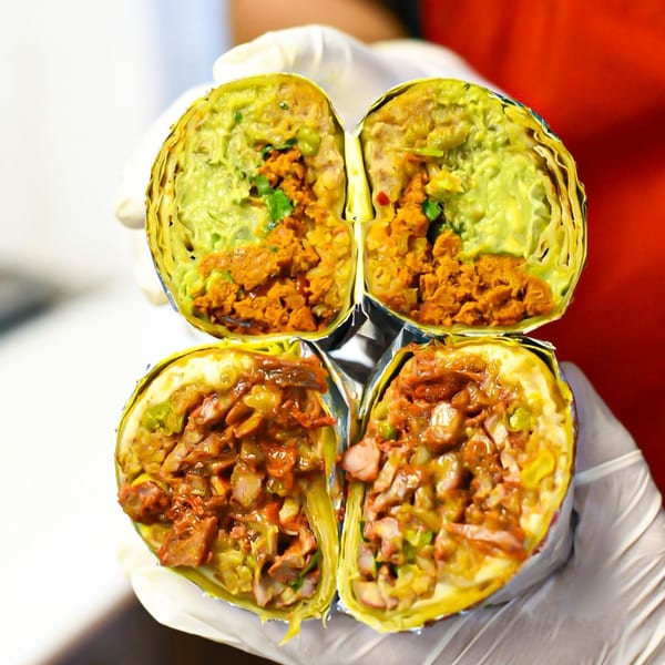 Two hands in white gloves hold two burritos, each cut in half, revealing meat and guacamole.